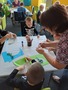 U stolu sedí tři děti, které z papírových talířů a barevných papírů vyrábí medúzy. Stojí u nich paní knihovnice a pomáhá jim.
