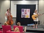 Na pódiu v sále KKV vystupuje hudební duo Gábina a Katka, Gábina hraje na basu, Katka na kytaru.